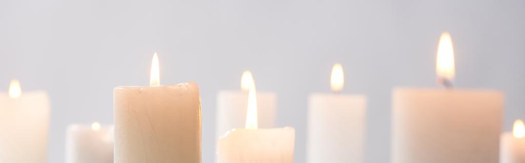 selektivní zaměření hoření bílých svíček zářících izolovaně na šedém, panoramatickém snímku - Fotografie, Obrázek