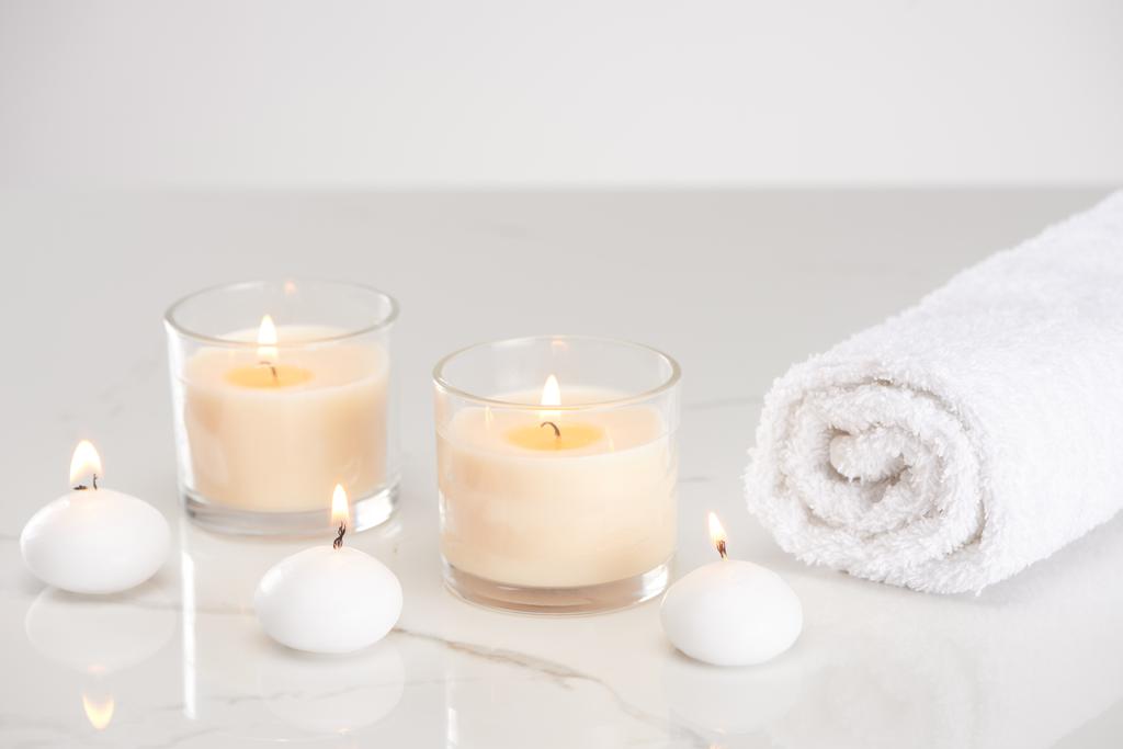 pálení bílých svíček ve skle a válcované ručník na mramorovém bílém povrchu - Fotografie, Obrázek