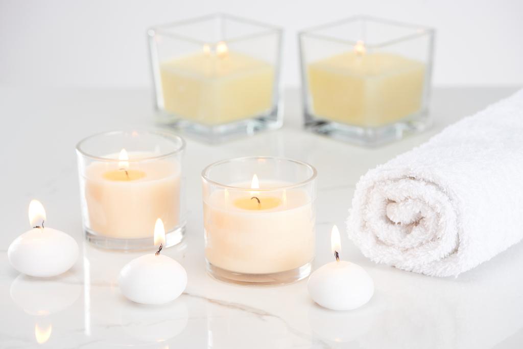 αναμμένα λευκά κεριά σε γυαλί και τυλιγμένη πετσέτα σε μαρμάρινη λευκή επιφάνεια - Φωτογραφία, εικόνα