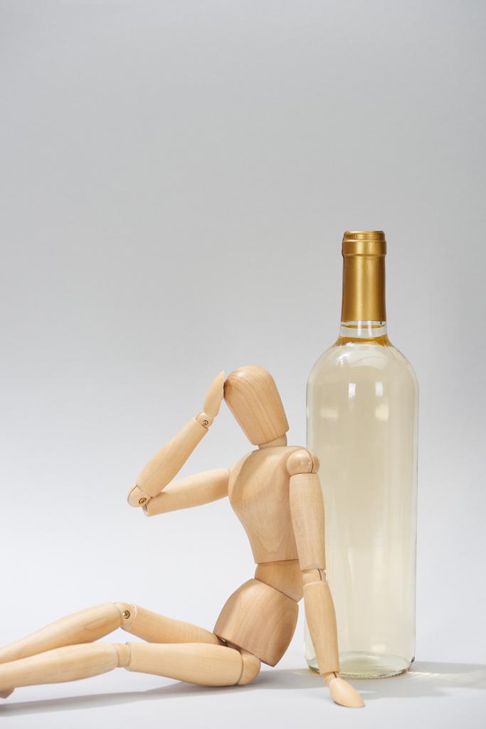 Dřevěná panenka s rukou po hlavě vedle vína láhev na šedém pozadí - Fotografie, Obrázek