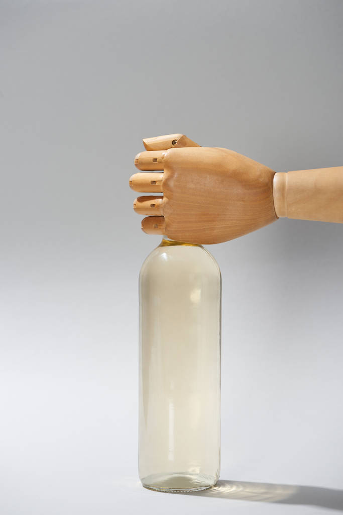 Mano de madera de maniquí con botella de vino sobre fondo gris
 - Foto, Imagen
