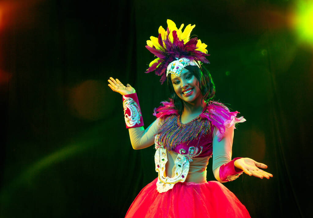 Όμορφη νεαρή γυναίκα σε καρναβάλι μάσκα και μεταμφίεση κοστούμι σε πολύχρωμα φώτα - Φωτογραφία, εικόνα