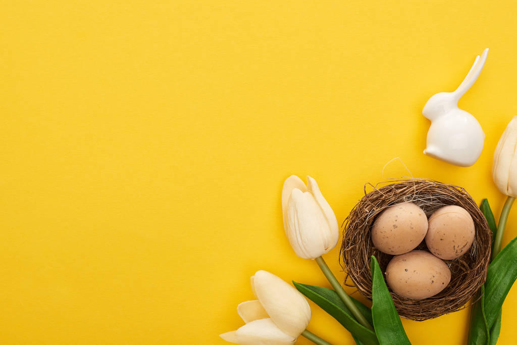 felső nézet tulipán és csirke tojás fészekben közel húsvéti nyuszi színes sárga háttér - Fotó, kép