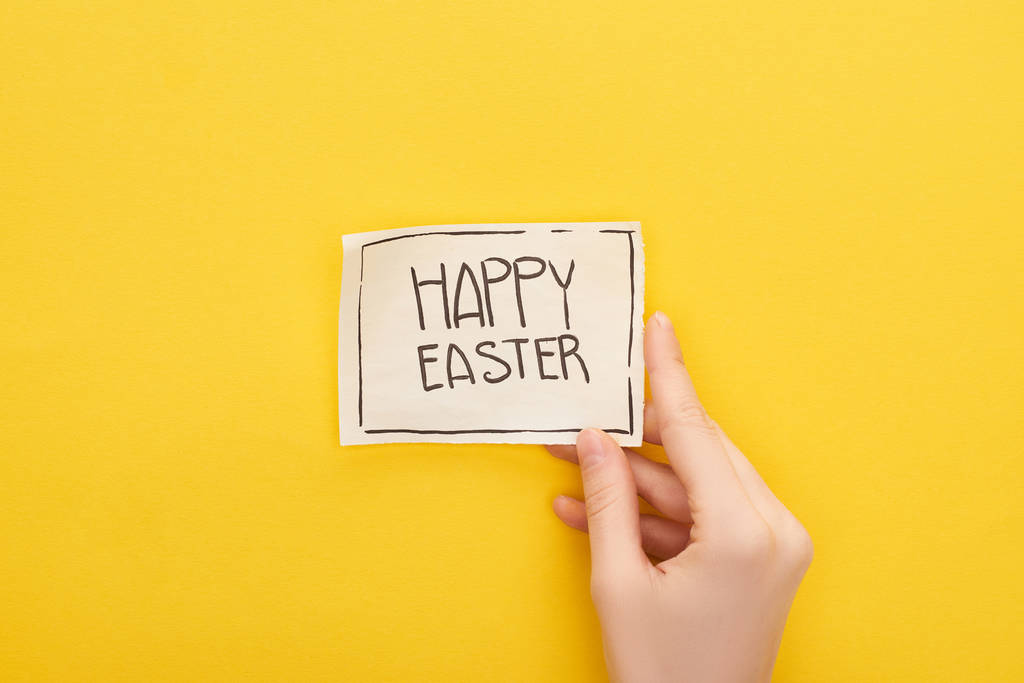 vista recortada de la mujer que sostiene la tarjeta de felicitación con letras de Pascua feliz sobre fondo amarillo
 - Foto, Imagen