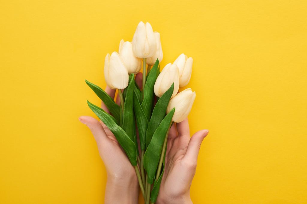 cropped view of woman holding spring tulips on colorful yellow background - Photo, Image