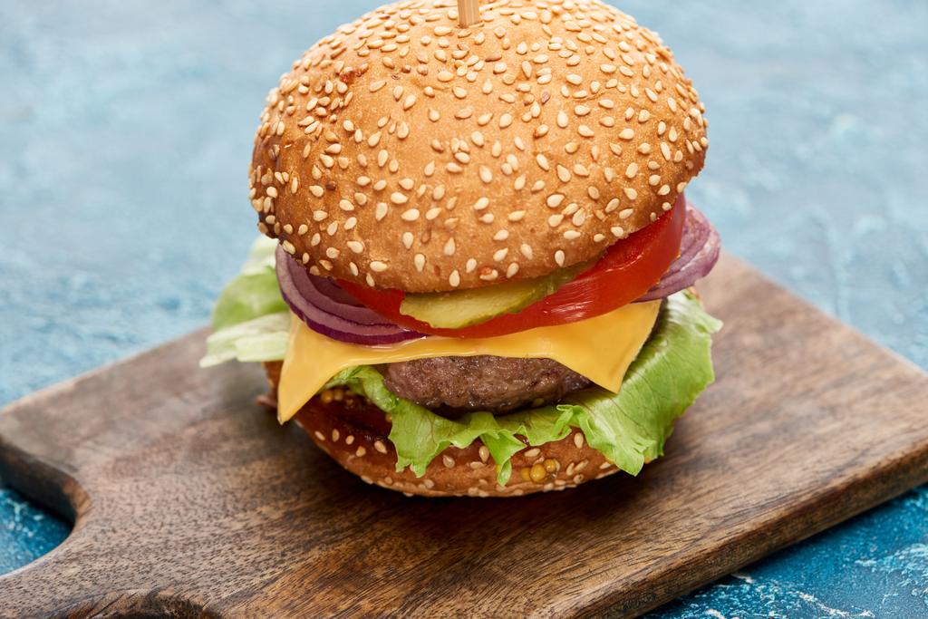 deliciosa hamburguesa con queso sobre tabla de madera sobre superficie de textura azul
 - Foto, imagen