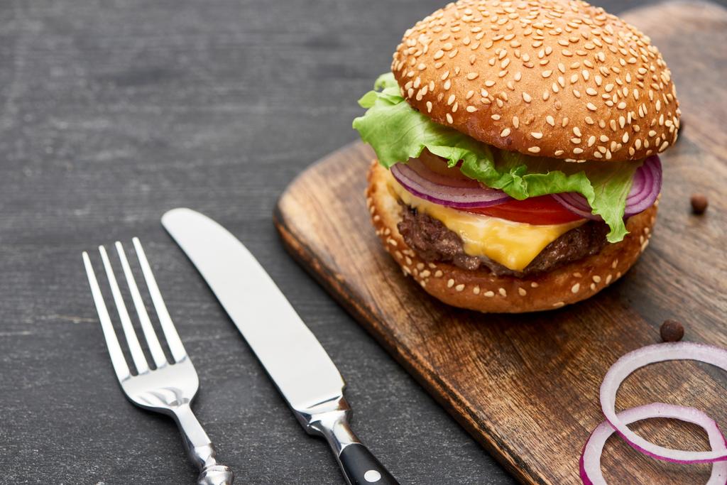 вкусный свежий чизбургер на деревянной доске возле столовых приборов
 - Фото, изображение