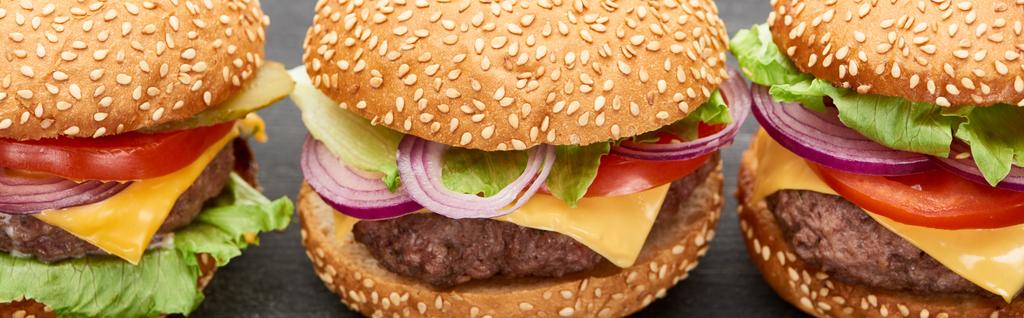 zblízka pohled na lahodné čerstvé cheeseburgery na černém stole, panoramatický záběr - Fotografie, Obrázek