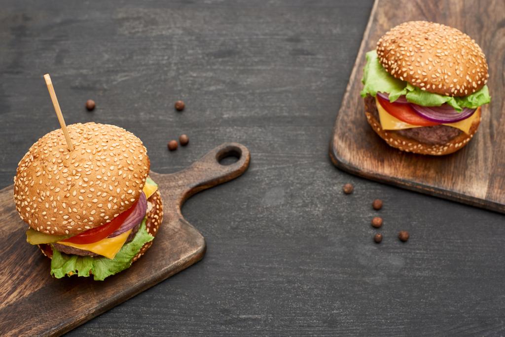 smakelijke verse cheeseburgers op houten planken op zwarte tafel - Foto, afbeelding