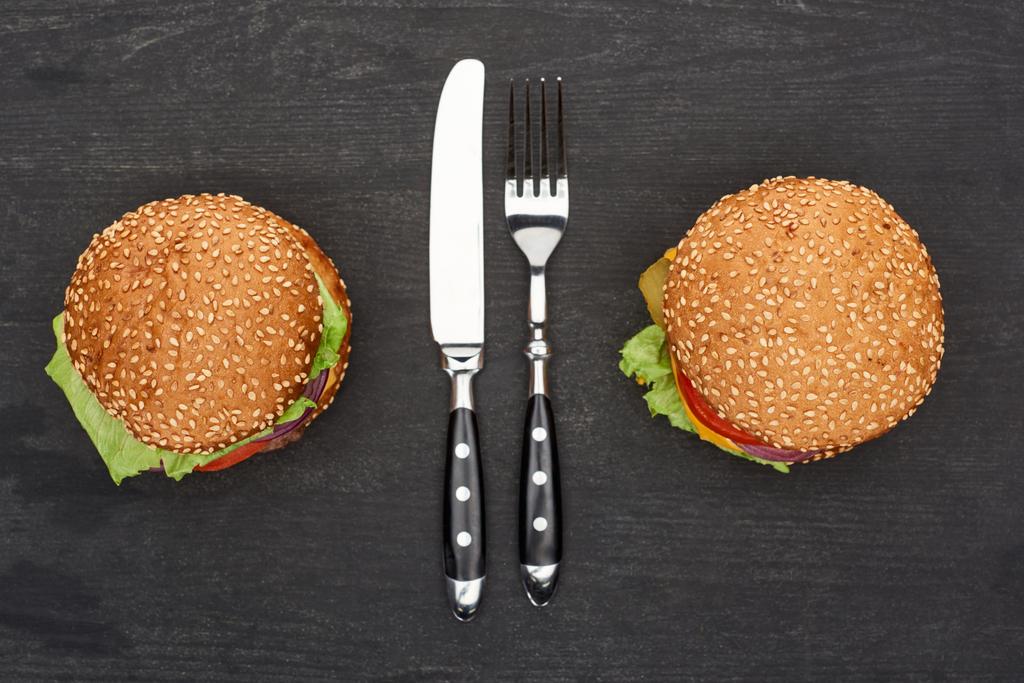 Tahta siyah masada çatal bıçaklı lezzetli taze hamburgerler. - Fotoğraf, Görsel