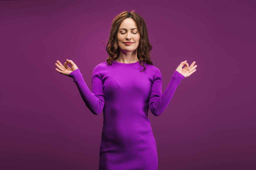 pozytywna kobieta medytująca z zamkniętymi oczami na fioletowym tle - Zdjęcie, obraz