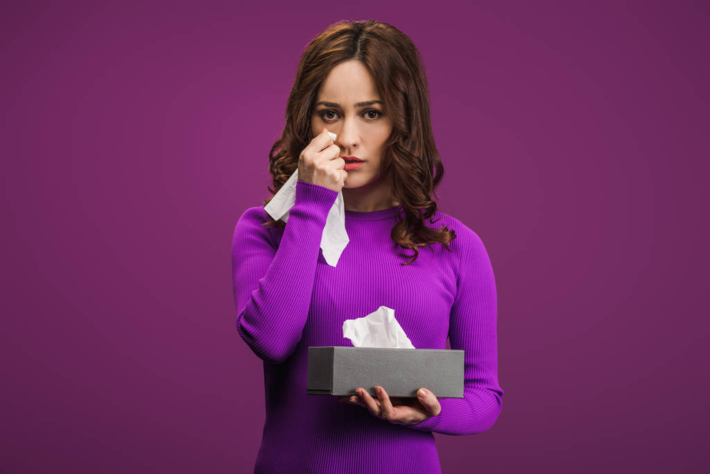 mujer triste limpiando lágrimas con servilleta de papel mientras llora sobre fondo púrpura
 - Foto, Imagen