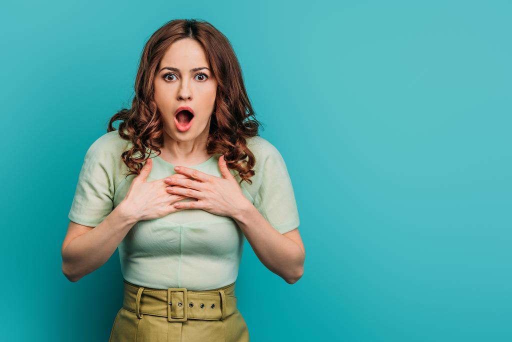 schockierte Frau hält Hände auf Brust, während sie mit offenem Mund vor blauem Hintergrund steht - Foto, Bild