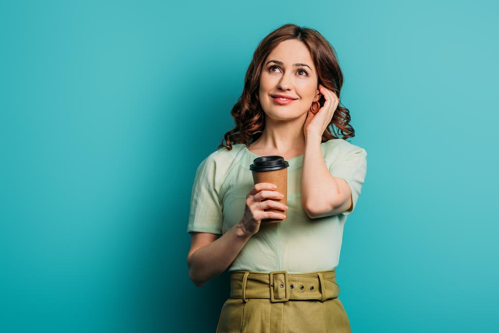 verträumtes Mädchen schaut auf, während es Kaffee hält, um auf blauem Hintergrund zu gehen - Foto, Bild