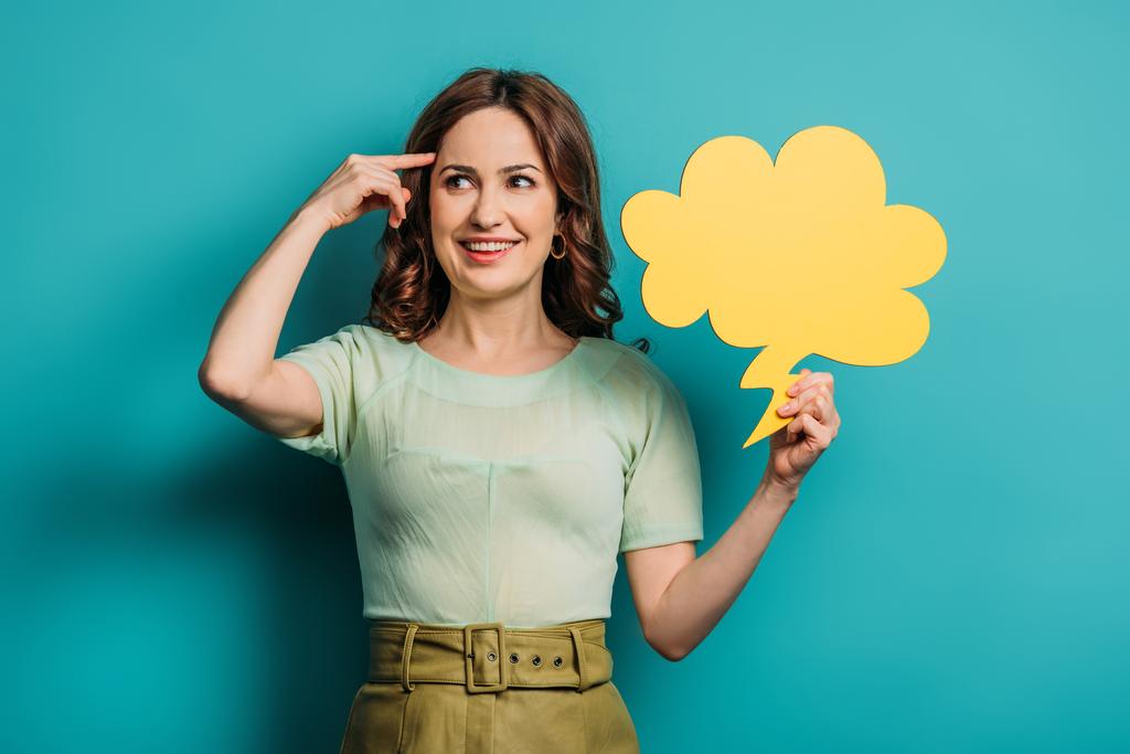cheerful woman showing idea sign while holding thought bubble on blue background - Photo, Image