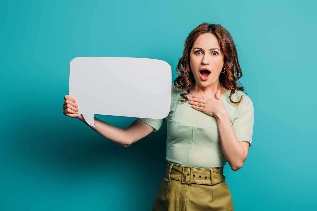 shocked woman touching chest while holding speech bubble on blue background - Photo, Image
