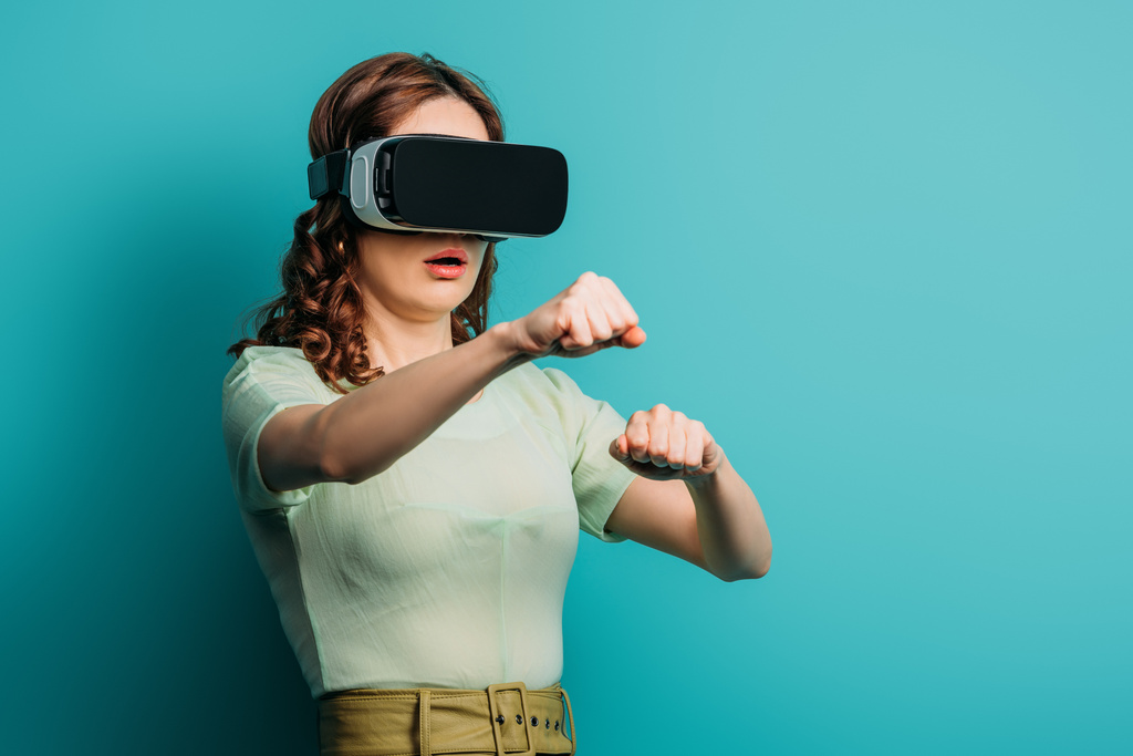 surprised girl in vr headset imitating fighting on blue background - Photo, Image