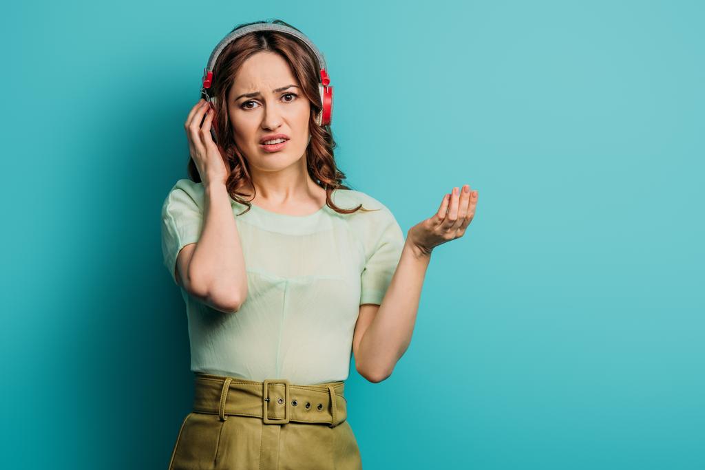 fille mécontente dans les écouteurs sans fil debout avec bras ouvert sur fond bleu
 - Photo, image
