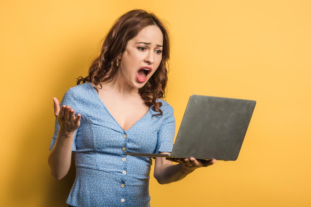 Sarı arka planda dizüstü bilgisayarda görüntülü sohbet sırasında bağıran kızgın kadın. - Fotoğraf, Görsel