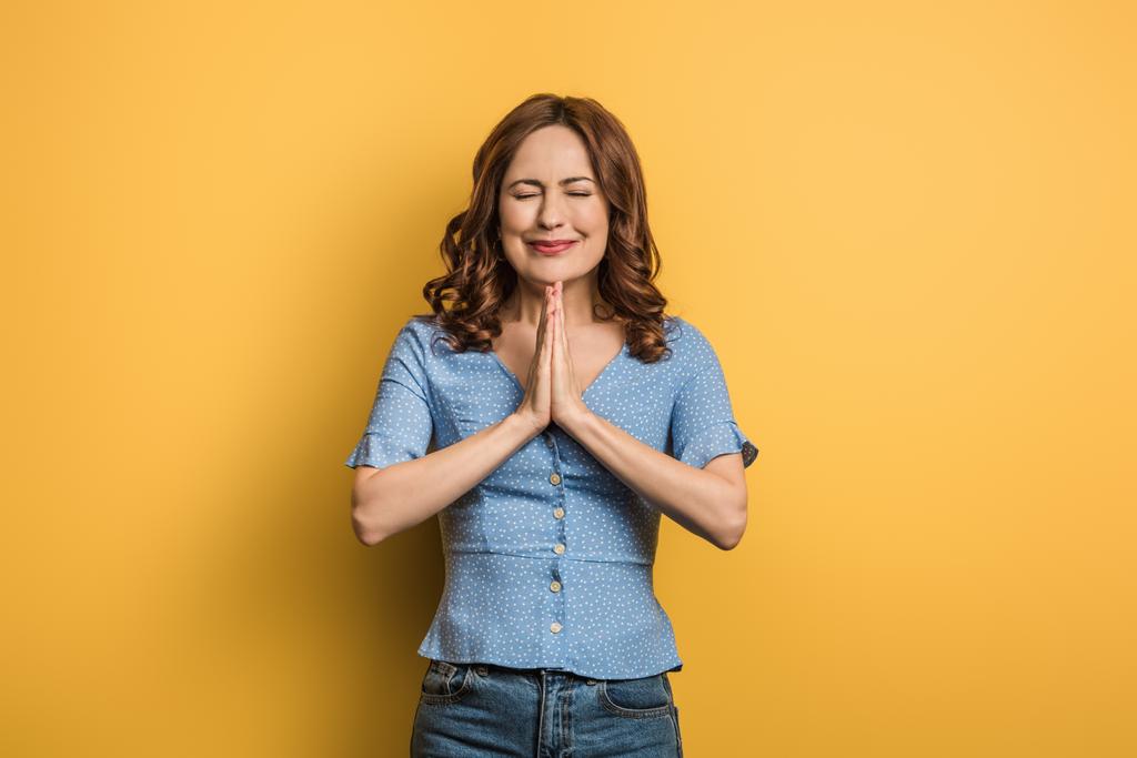 anxious girl showing praying hands with closed eyes on yellow background - Photo, Image
