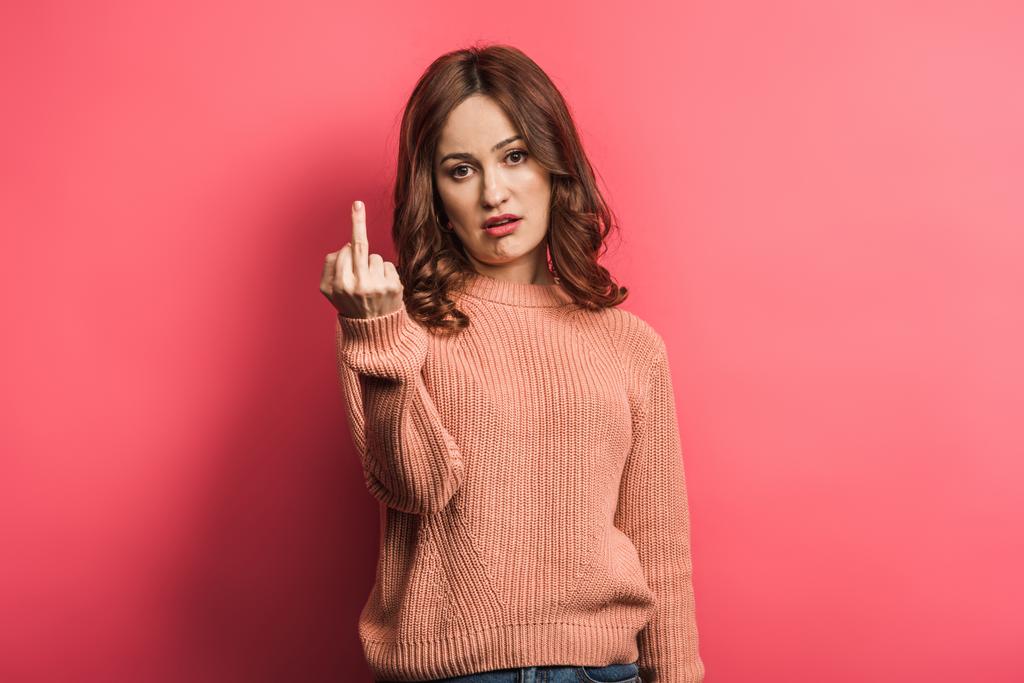 displeased girl looking at camera and showing middle finger on pink background - Photo, Image