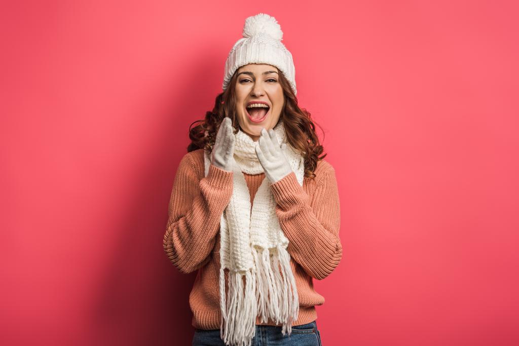 fröhliches Mädchen mit warmer Mütze und Schal lacht in die Kamera auf rosa Hintergrund - Foto, Bild
