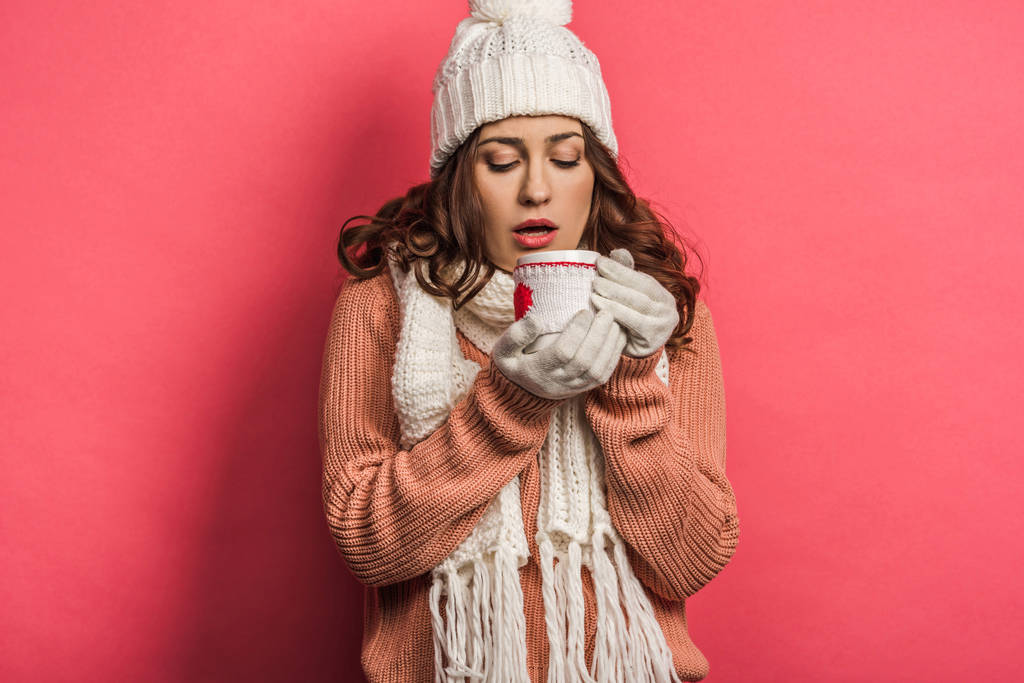 fille froide en chapeau chaud et écharpe tenant tasse avec boisson chauffante sur fond rose
 - Photo, image