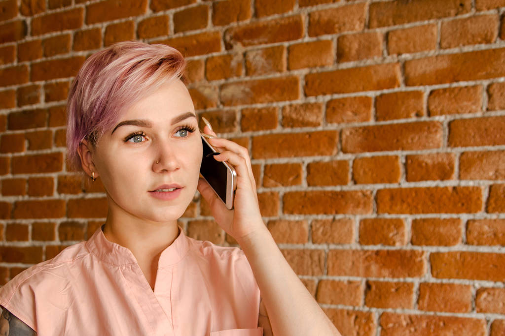 Joven hermosa chica está hablando en el teléfono móvil en un fondo de pared de ladrillo
 - Foto, imagen