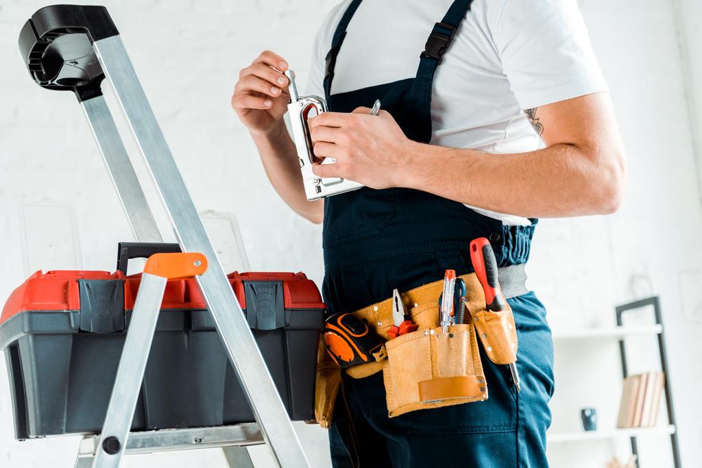 обрезанный вид монтажника с инструментальным ремнем, держащим строительный степлер
  - Фото, изображение