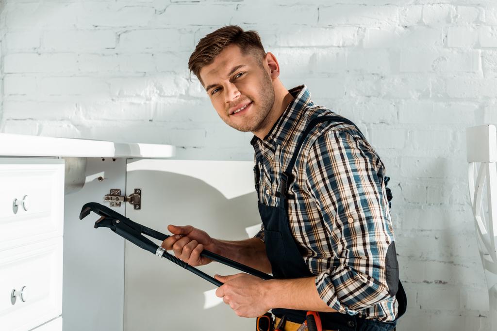 gelukkig installateur houden slip joint tangen tijdens het werken in de buurt keuken kast  - Foto, afbeelding