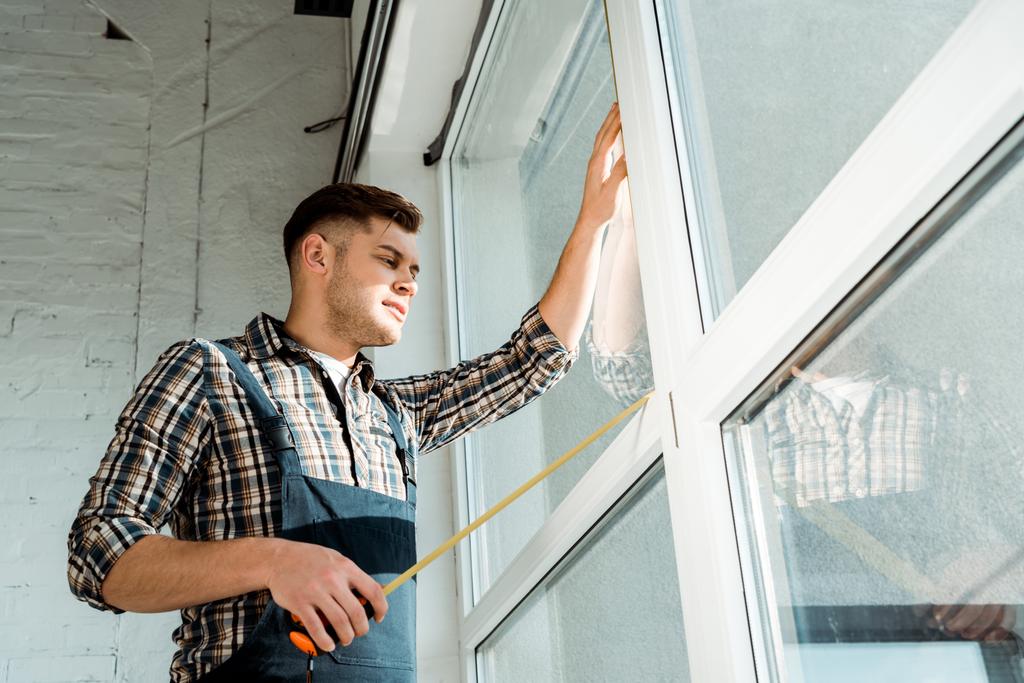 low angle view of installer standing near windows and holding measuring tape - Photo, Image