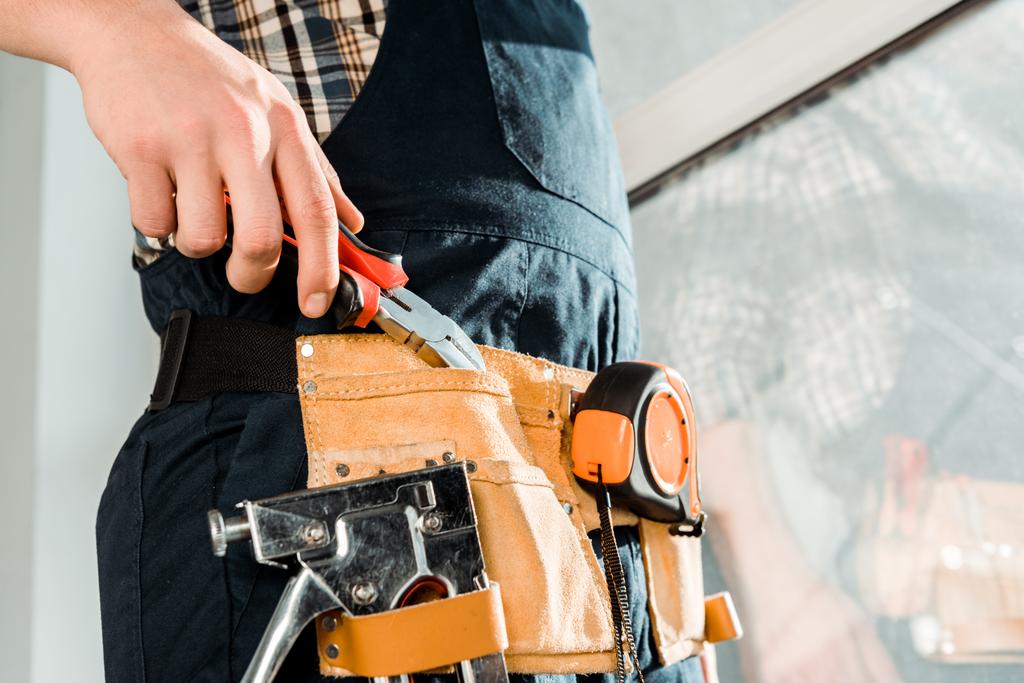 cropped view of installer in tool belt taking pliers  - Photo, Image