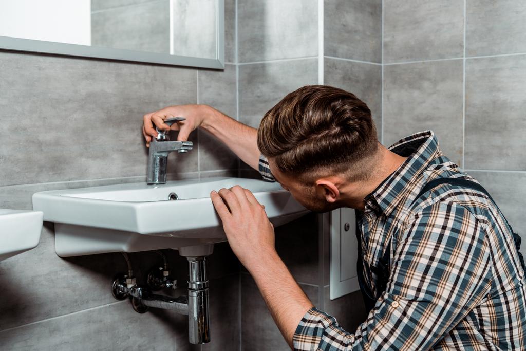 Установщик касаясь кран и белый раковина в ванной комнате
  - Фото, изображение