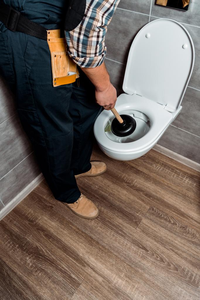 καλλιεργημένη άποψη του υδραυλικού που κρατά το έμβολο κοντά στη λευκή τουαλέτα  - Φωτογραφία, εικόνα