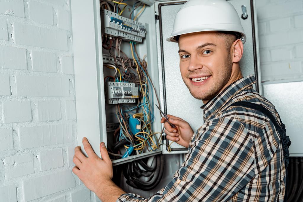 eletricista feliz no capacete de segurança segurando chave de fenda perto do quadro
   - Foto, Imagem