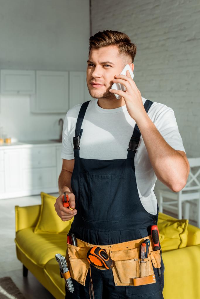 sunshine on handsome installer in overalls holding cutter and talking on smartphone  - Photo, Image