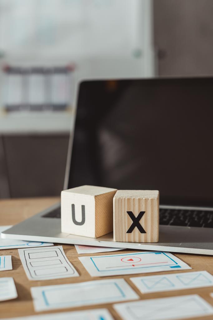 selektiver Fokus von Holzwürfeln mit UX-Buchstaben auf Laptop mit Designer-Skizzen auf dem Tisch - Foto, Bild