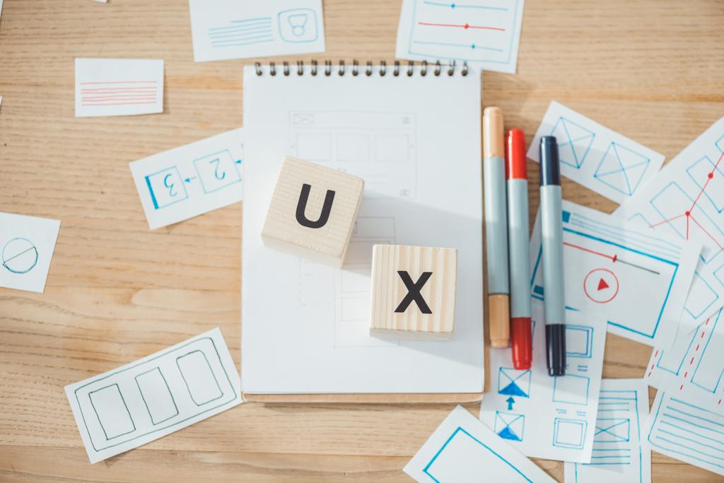Bovenaanzicht van kubussen met ux letters en website ux app ontwikkeling schetsen op houten tafel - Foto, afbeelding