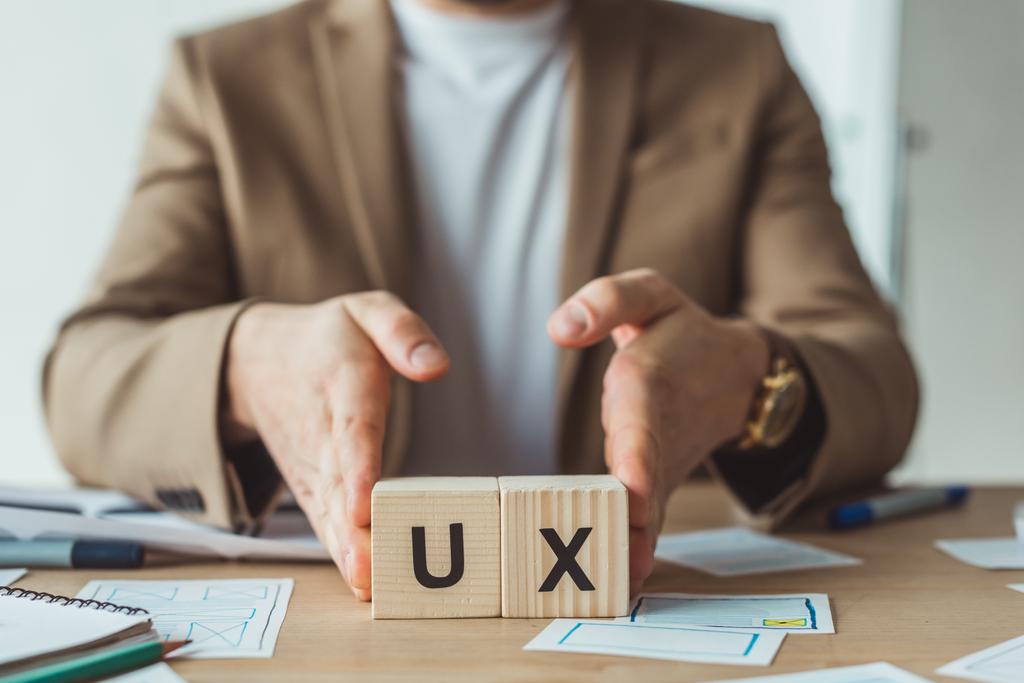 Cropped view of designer holding wooden cubes with ux letters at table with layouts - Photo, Image