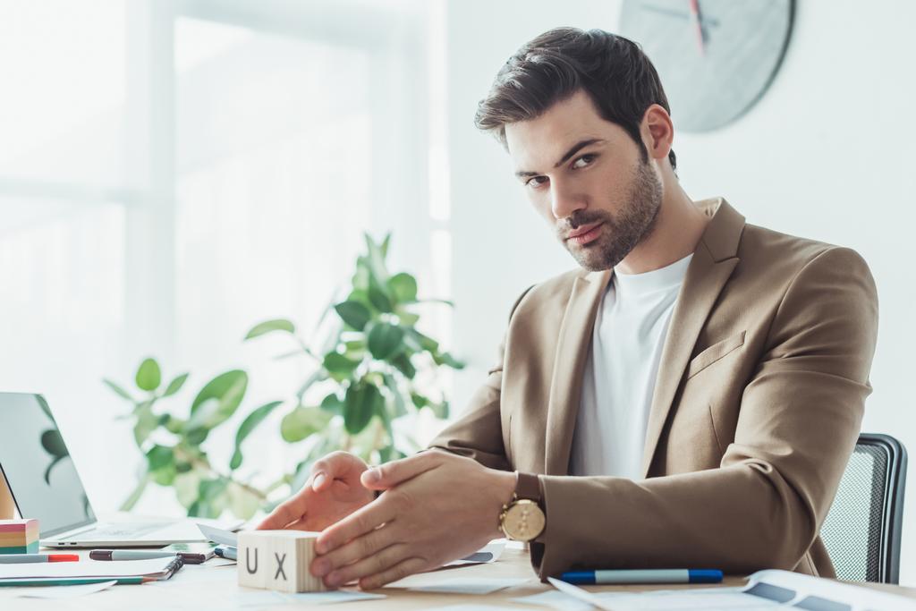 Handsome designer looking at camera while holding cubes with ux letters at working table - Photo, Image