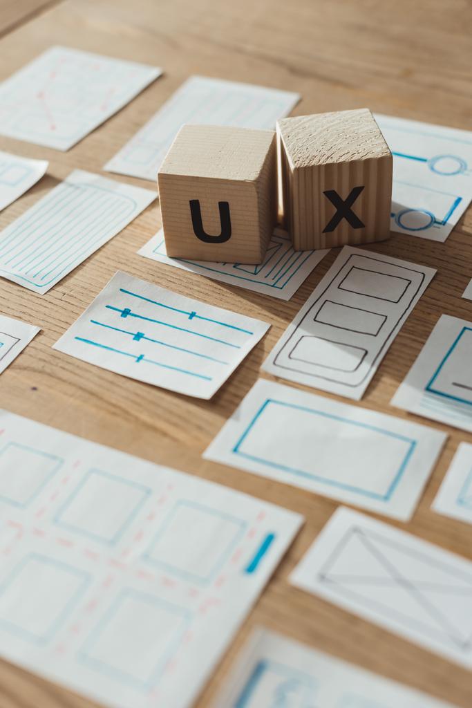 Selektive Fokussierung von Holzwürfeln mit UX-Buchstaben durch App-Skizzen auf dem Tisch  - Foto, Bild