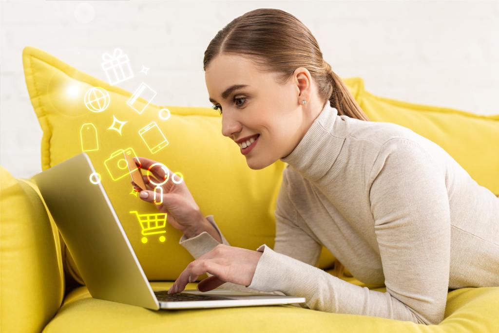 Vista lateral de la mujer sonriente usando el ordenador portátil y la celebración de la tarjeta de crédito junto a la ilustración
 - Foto, Imagen