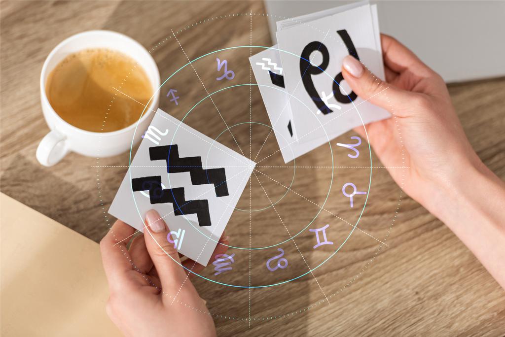 Καλλιεργημένη άποψη του αστρολόγου κρατώντας κάρτες με ζώδια εκτός από τον καφέ και την εικονογράφηση - Φωτογραφία, εικόνα