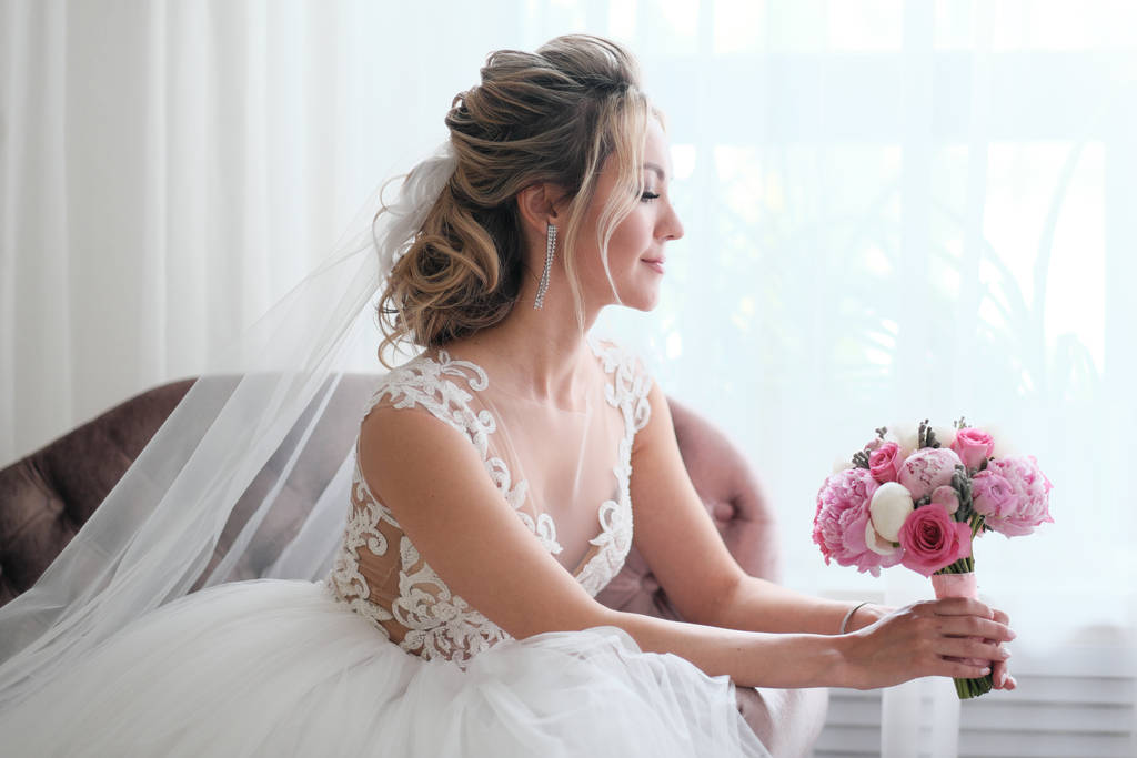 Csinos menyasszony szőke haj visel esküvői ruha és fátyol gazdaság virág csokor - Fotó, kép