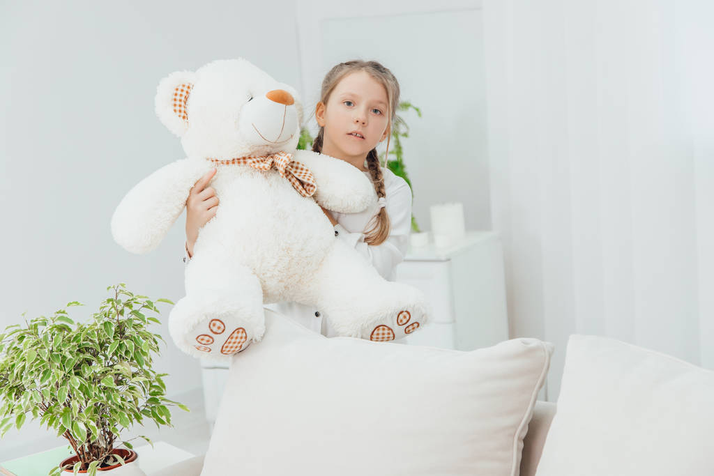 Adorable little girl standing with big white teddy-bear in her hands. A little bit worried face expression. - Photo, Image