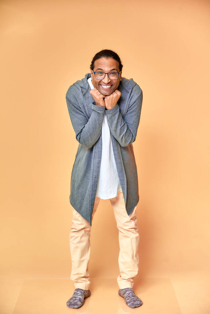 Retrato vertical de un joven alegre con gafas afroamericanas con un corte de pelo corto en ropa ordinaria sobre un fondo rosa en toda su longitud. De pie justo delante de la cámara
 - Foto, Imagen