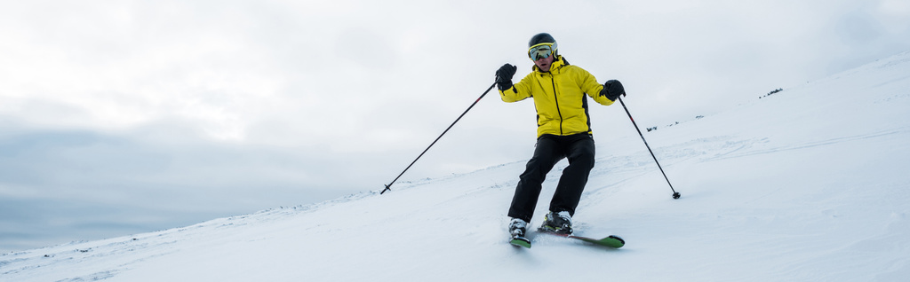 panoramic shot of man in helmet and goggles skiing on slope in wintertime - Photo, Image