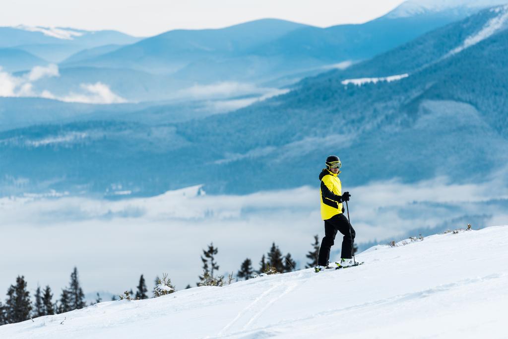 αθλητής στο κράνος κρατώντας μπαστούνια και σκι στην πλαγιά έξω - Φωτογραφία, εικόνα