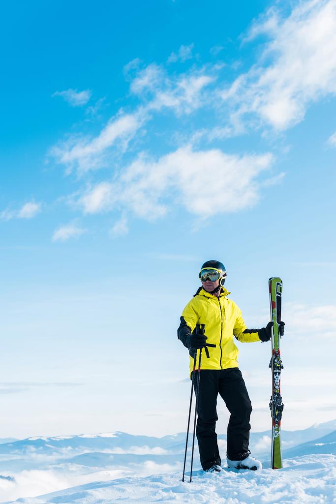  Kayak gözlüklü kayakçı elinde kayak çubuklarıyla mavi gökyüzüne karşı karda duruyor. - Fotoğraf, Görsel