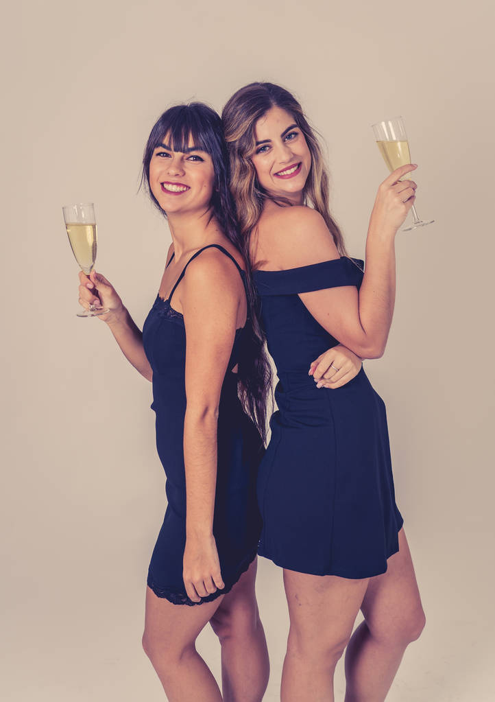 Dos hermosas novias que se divierten celebrando la Navidad o Año Nuevo gafas de brindis. Las mujeres posando en vestidos de fiesta sexy con estilo beber champán. Gente Amistad y celebración. - Foto, imagen